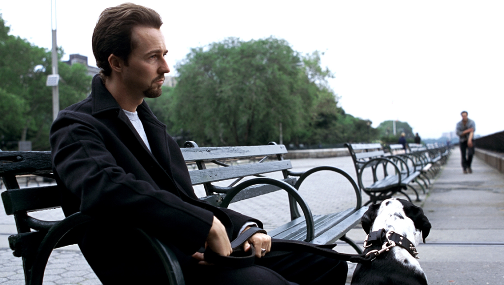 Edward Norton in Spike Lee's *25th Hour*. Norton sits on a bench with his dog in NYC. Drama film.