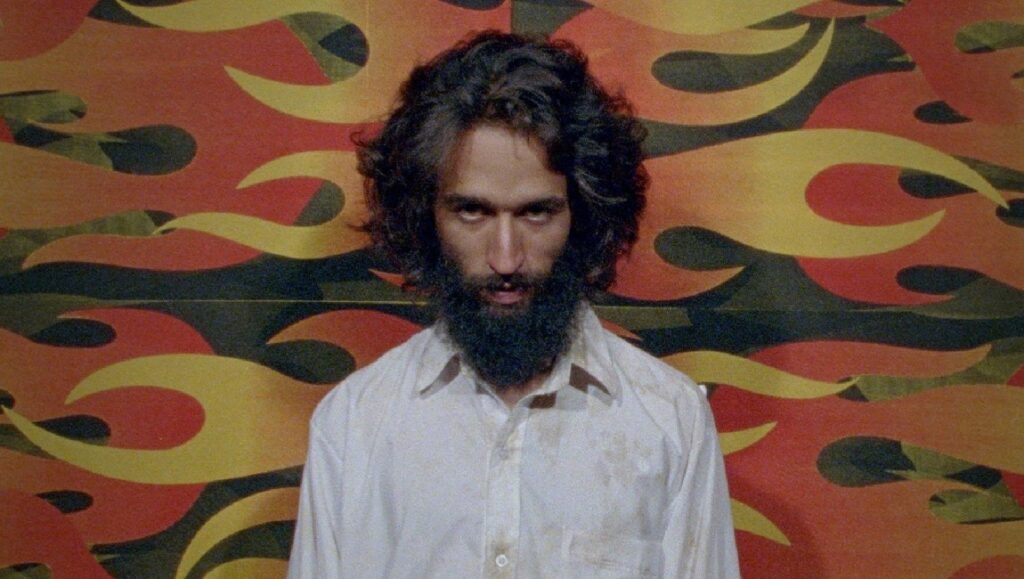 Camilo Restrepo's Los Conductos film still. Man with beard, white shirt, and flame-like background. Indie film.