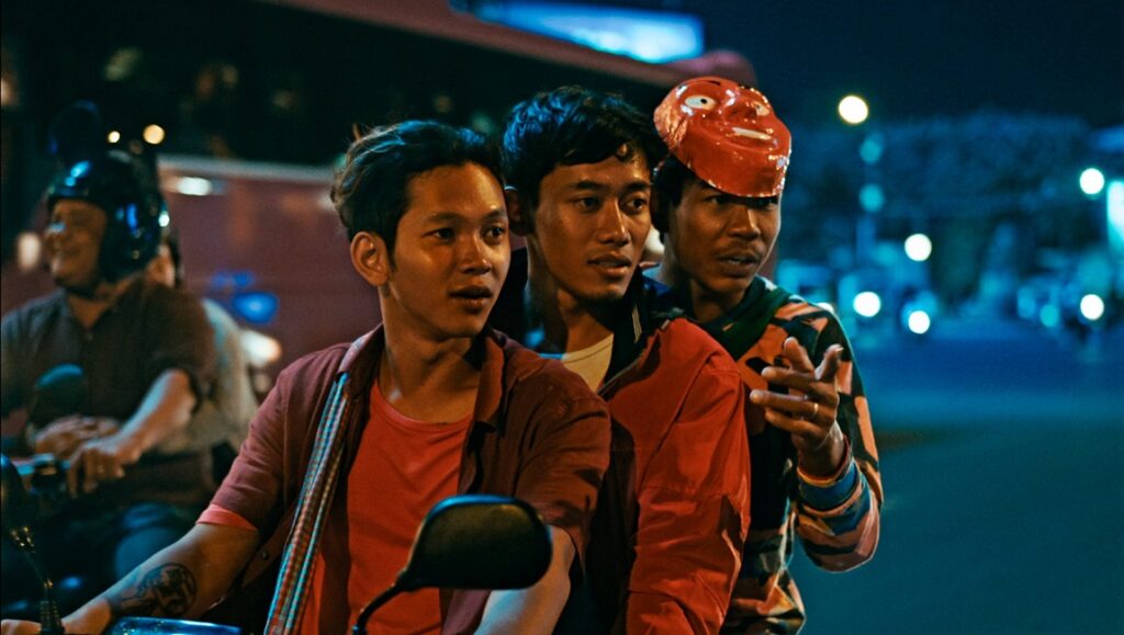 White Building — Kavich Neang White Building film still. Three young men on a motorbike, one wearing a red mask. New Directors/New Films 2022.