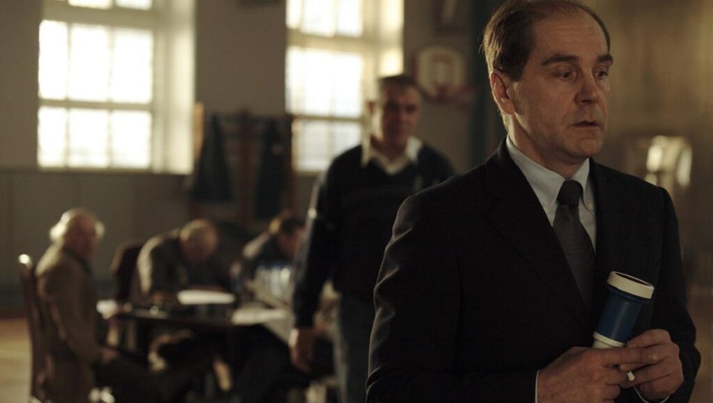 Nikita Mikhalkov in 12 movie. Man in suit holds gavel, jurors in background. Drama film scene.