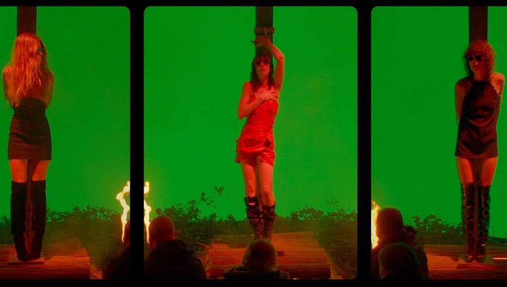 Lux Æterna — Gaspar Noé Lux Æterna film still. Three women tied to stakes against a green screen, flames below. Gaspar Noé movie.