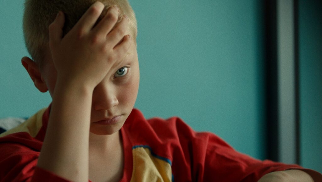 The Worst Ones — Lise Akoka & Romane Gueret The Worst Ones movie still: Young boy with hand on head, looking pensive. Lise Akoka & Romane Gueret film.