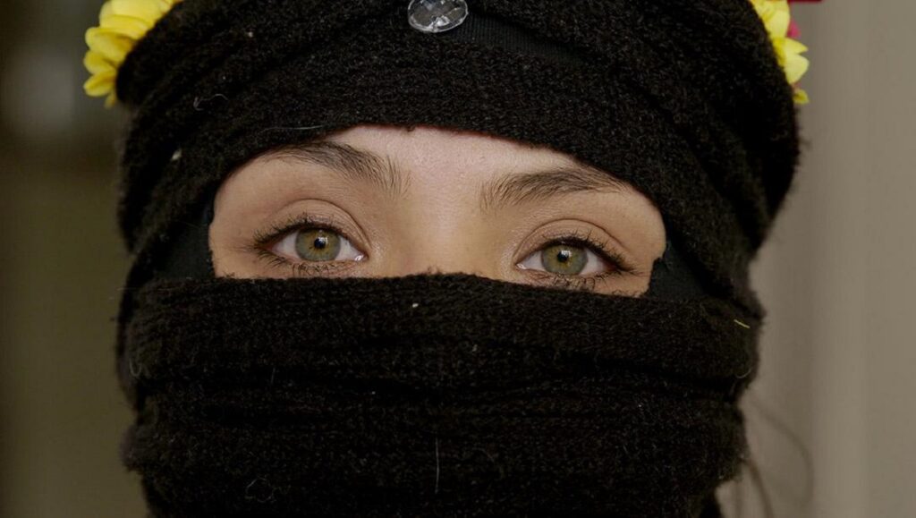 My Imaginary Country — Patricio Guzmán Close-up of woman's eyes in My Imaginary Country. Black head covering, yellow flowers. Patricio Guzmán film.
