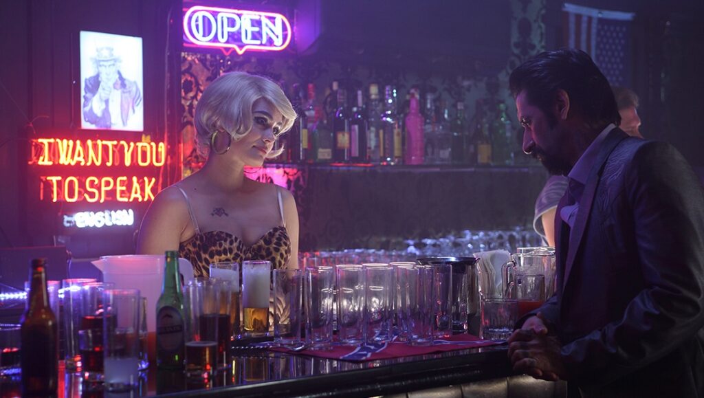 There Are No Saints film scene: Woman bartender, man in suit at bar. Neon signs, bottles, and glasses.
