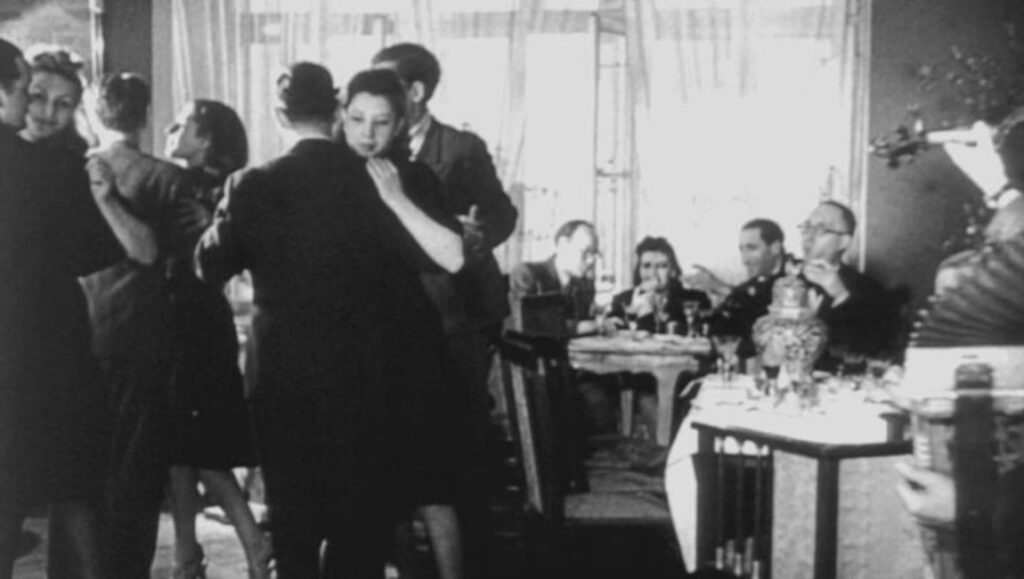 Black and white film still. People dance while others dine and listen to music. Vintage party scene.