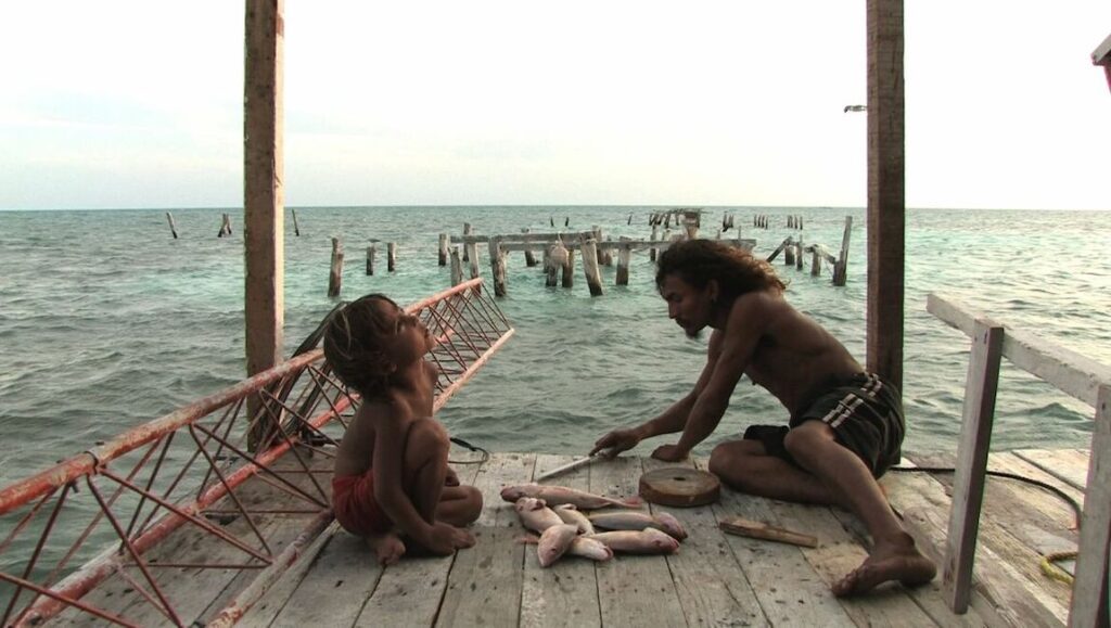 Indigenous man and child preparing fish on a wooden platform over the ocean. Fishing lifestyle.