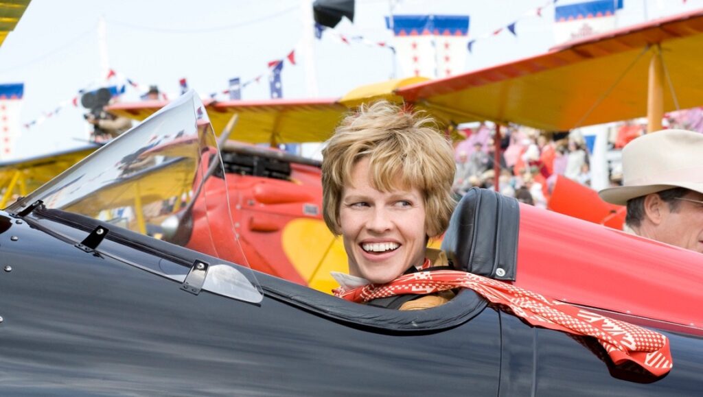 Amelia — Mira Nair Hilary Swank as Amelia Earhart in Amelia movie. Pilot smiling in vintage airplane cockpit. Mira Nair film.