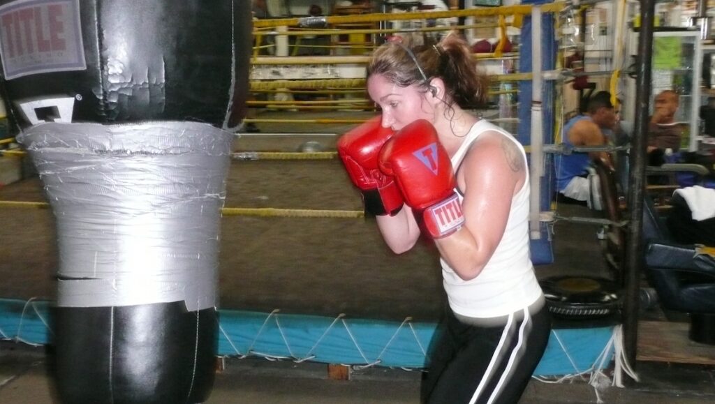 Boxing Gym — Frederick Wiseman Woman boxing. Female boxer training with red gloves at the gym, punching a heavy bag. Boxing workout.