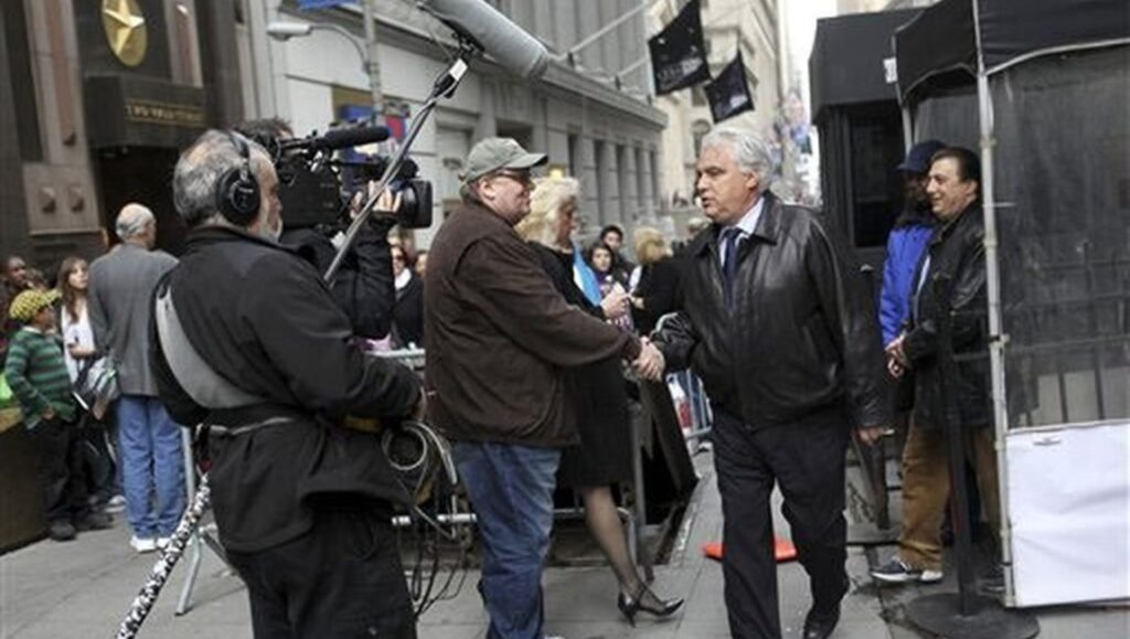 Michael Moore filming Capitalism: A Love Story with a camera crew. Two men shake hands on a city street.