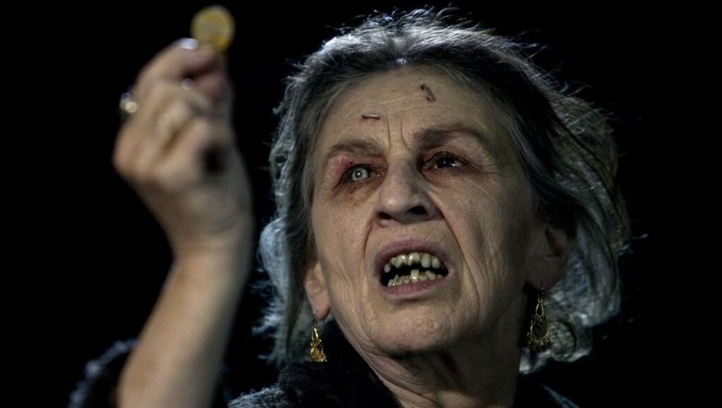 Drag Me to Hell movie scene: An old, scary woman holds a coin. Horror film character with eerie makeup.