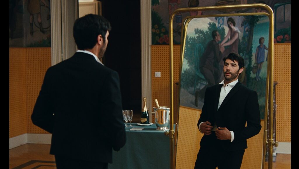 Don Juan — Serge Bozon Man in suit looks in mirror. Champagne, glasses on table. Formal wear, fashion.