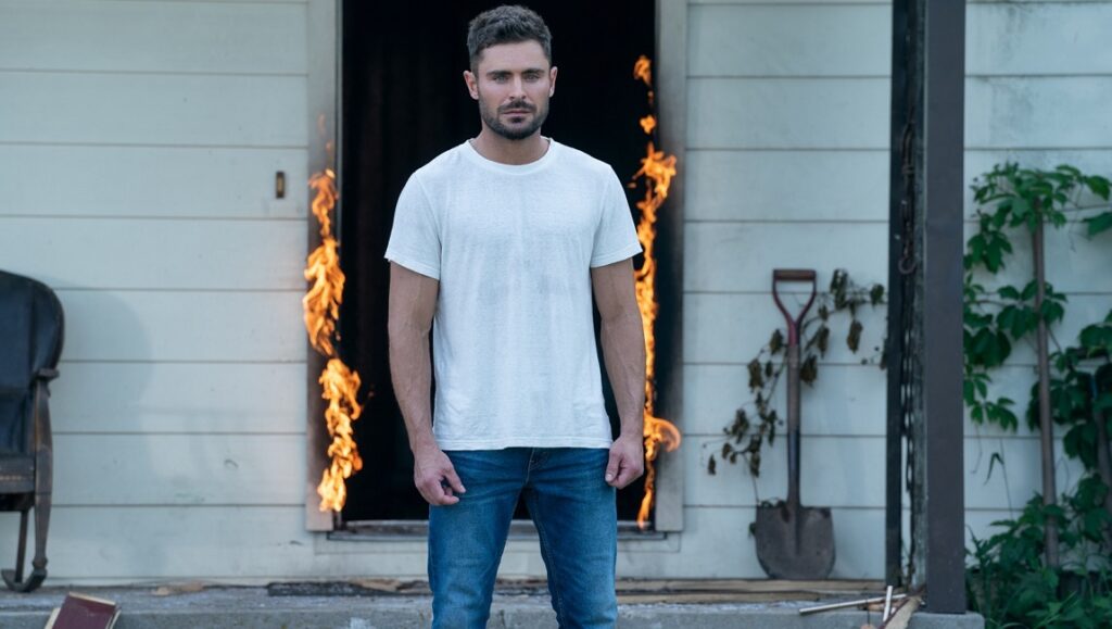 Zac Efron in Firestarter. Man stands in front of burning doorway. Firestarter movie.