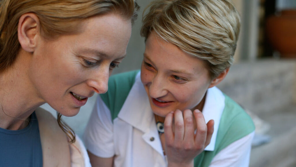 Two women, one with short blonde hair, looking down and smiling. People, friendship, and lifestyle.