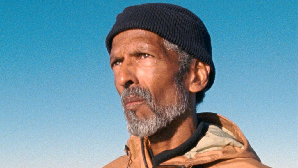 Erika Etangsalé's In the billowing night features a man in a beanie and jacket against a blue sky.