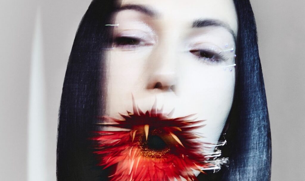 Kelly Lee Owens — LP.8 Kelly Lee Owens album art. Singer with dark hair, red flower in mouth. April 2022 music roundup.