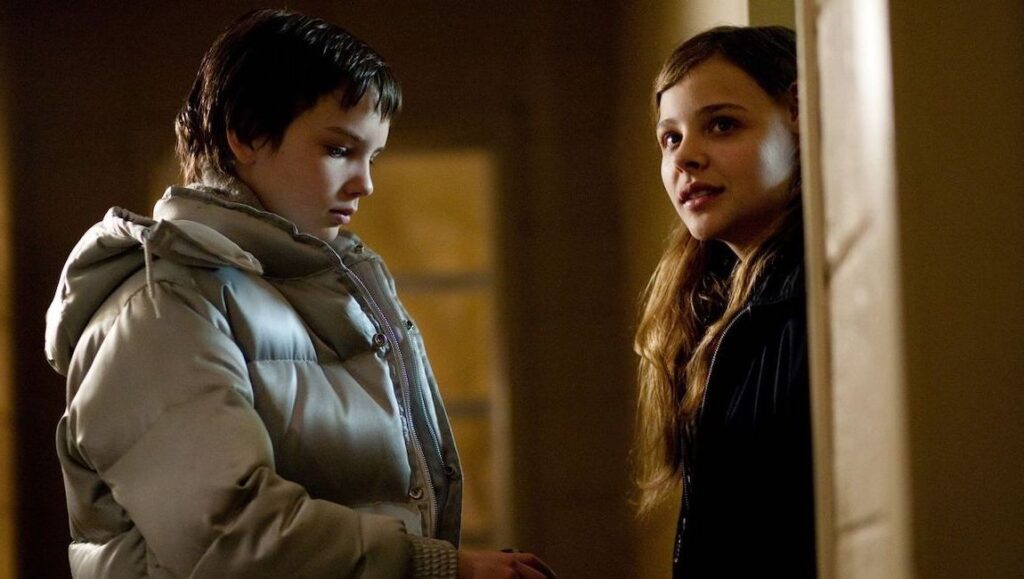 Let Me In — Matt Reeves Let Me In movie scene: Kodi Smit-McPhee and Chloë Grace Moretz in a tense moment. Horror film.