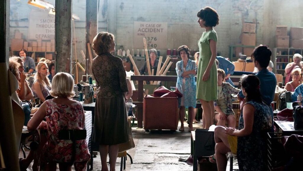 Made in Dagenham — Nigel Cole Made in Dagenham movie scene. Women factory workers in dresses, vintage setting, sewing machines. Film still.