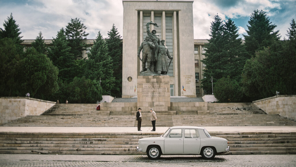 Metronom — Alexandru Belc Scene from Metronom at Cannes Film Festival 2022. Car, statue, and two men on steps.
