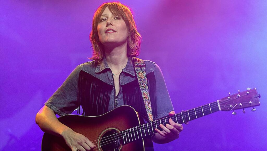 Molly Tuttle — Crooked Tree Molly Tuttle, April 2022 album. Singer-songwriter performing with acoustic guitar. Fringe denim jacket, floral strap.