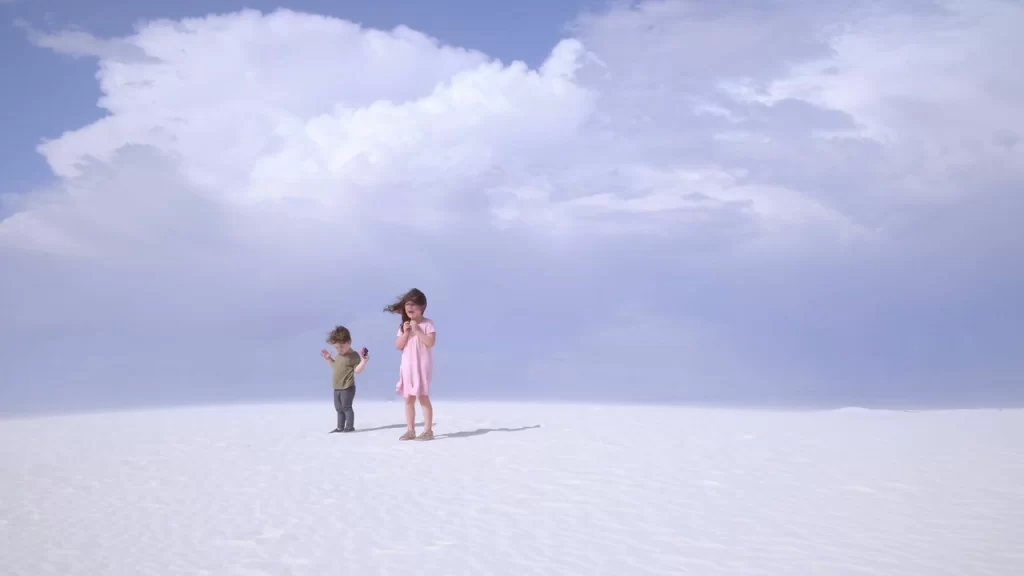 Nuclear Family: Two children stand in a white landscape under a cloudy sky. Prismatic Ground 2022.