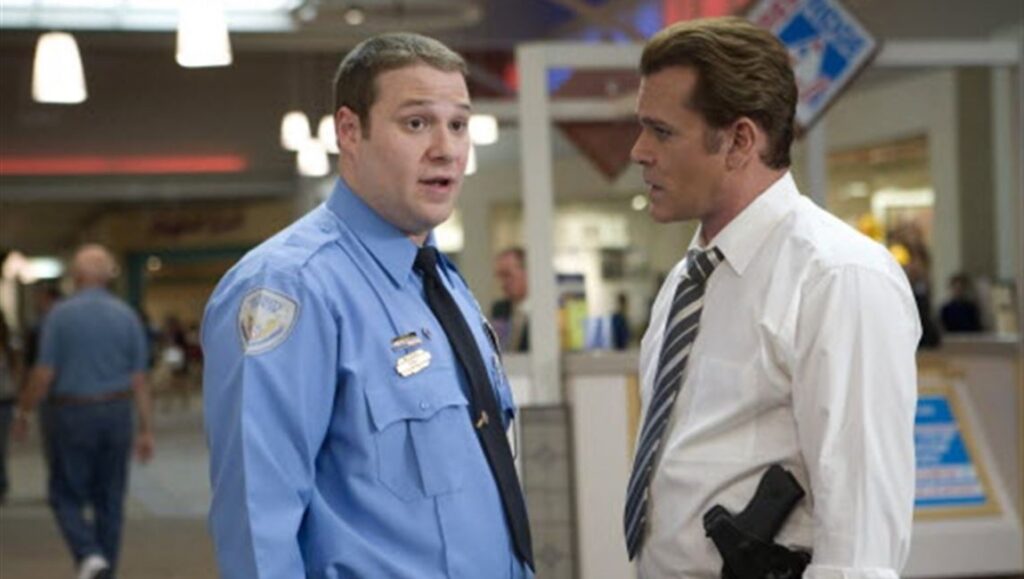 Observe and Report movie still. Seth Rogen as a mall security guard talks to a detective with a gun in a mall.