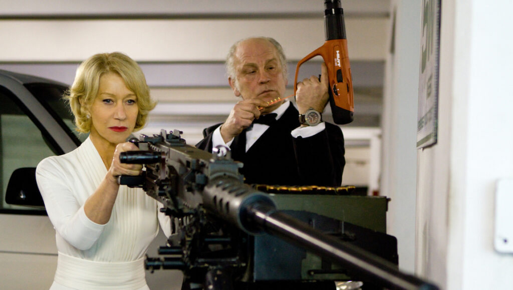 Helen Mirren and John Malkovich in RED. Mirren aims a machine gun, Malkovich holds a nail gun. Action movie.
