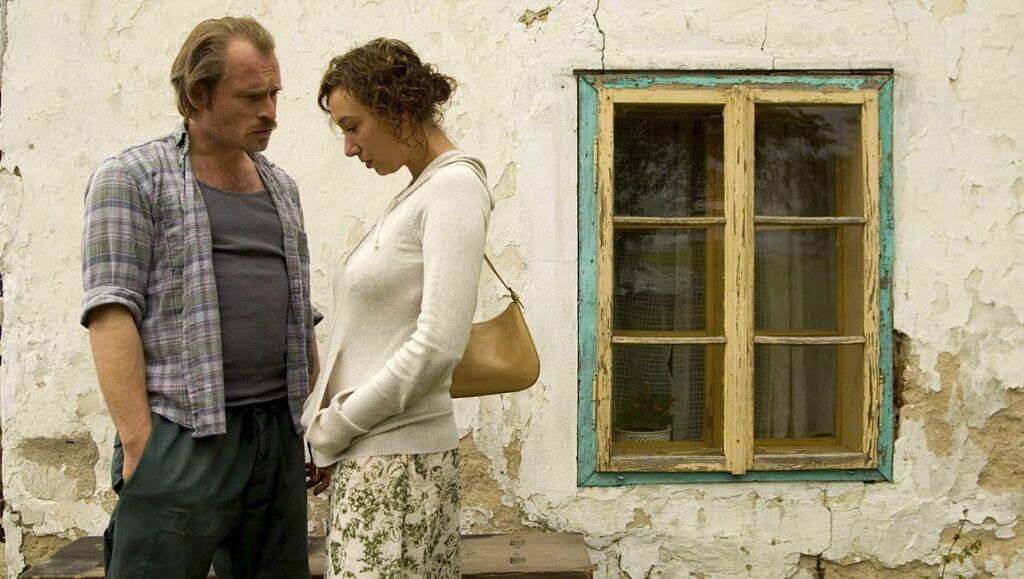Gotz Spielmann's Revanche film still. Man and woman stand near a weathered building with a window.