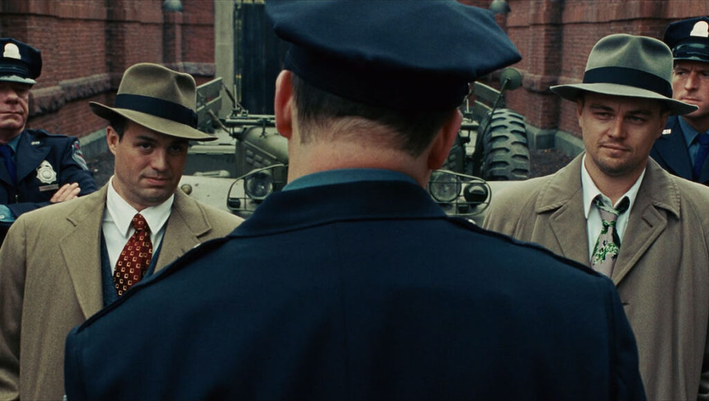 Shutter Island movie scene. Leonardo DiCaprio and Mark Ruffalo, detectives in hats, face a police officer. Thriller film.