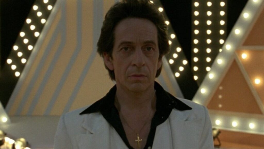 Tony Manero film still. Pablo Larraín's Tony Manero character in a white suit with a cross necklace.