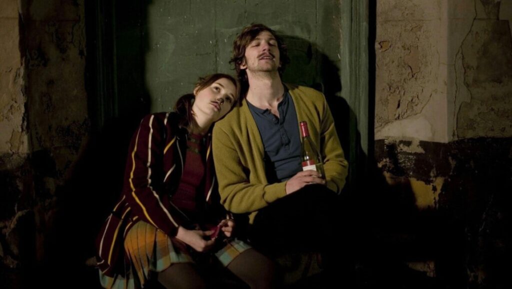 Couple with wine bottle relaxing against a textured wall. Casual fashion, dark setting.