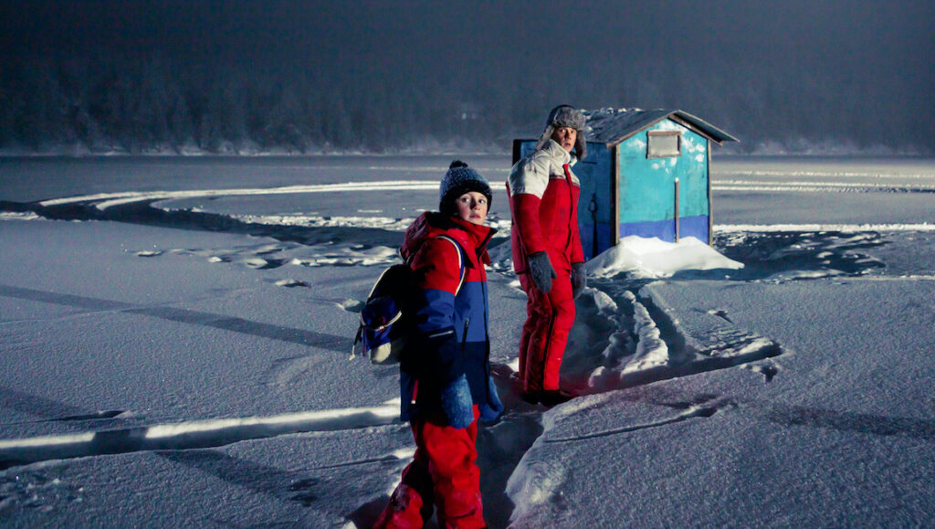 The Woodcutter Story — Mikko Myllylahti Still from Cannes Film Festival's Woodcutter's Story. Two figures stand on a snowy, icy landscape near a small blue shack.