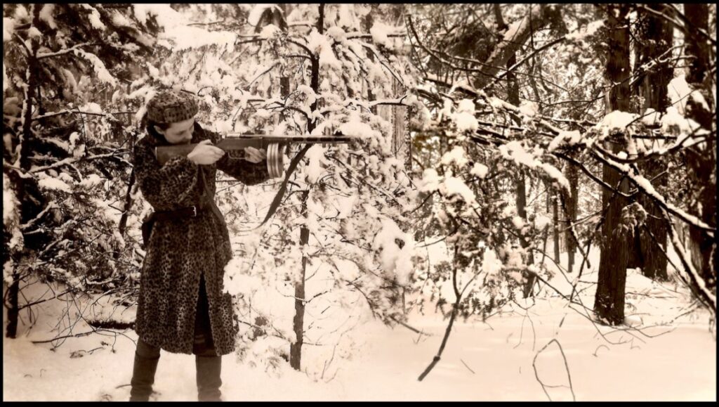 Four Winters film still. Woman with rifle in snowy woods. World War II movie scene. Sepia-toned image.