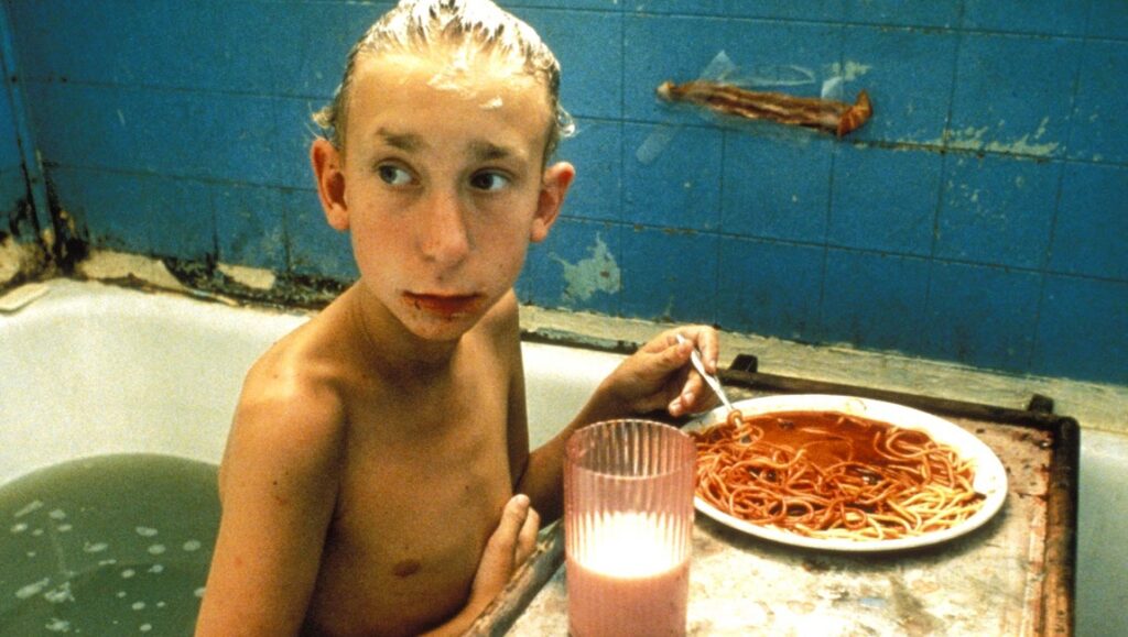Gummo — Harmony Korine Gummo film still: Boy in bathtub with spaghetti, pink drink, and dirty blue tiles.