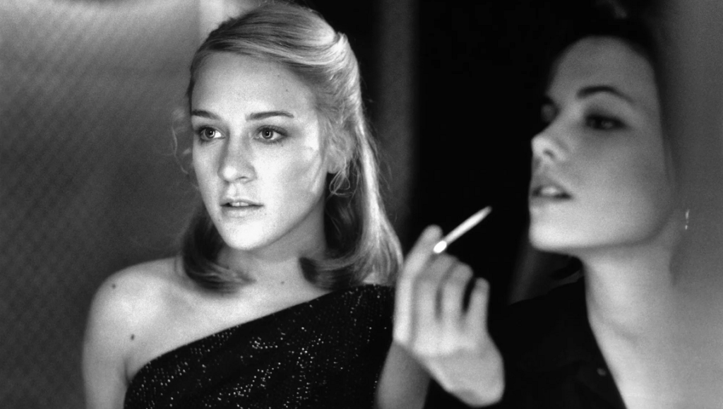 Black and white photo of Chloë Sevigny in The Last Days of Disco, smoking. Disco era film still.