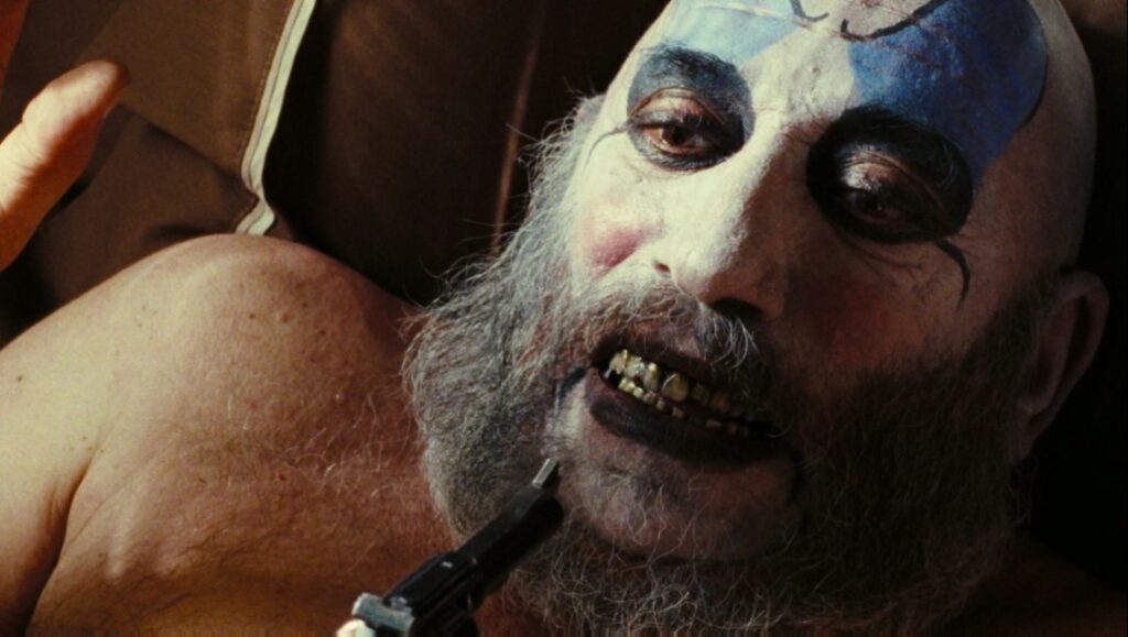 The Devil’s Rejects — Rob Zombie The Devil's Rejects still. Sid Haig as Captain Spaulding with clown makeup and a gun to his mouth. Rob Zombie horror film.