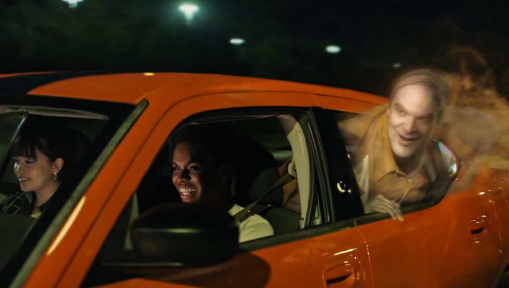 We Have a Ghost — Christopher Landon We Have a Ghost movie scene. Two people in a car with a ghost peering out the window. Netflix film.