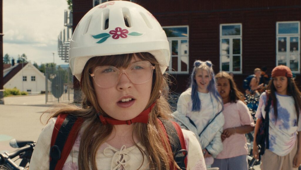 Dancing Queen movie still. Girl with helmet, glasses, and backpack. Friends in background.