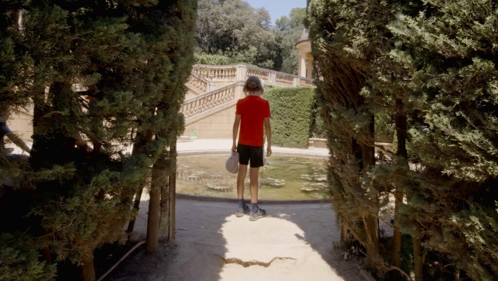 Boy in red shirt stands at Laberint d'Horta park entrance, Barcelona. Garden labyrinth view. Tourist attraction.