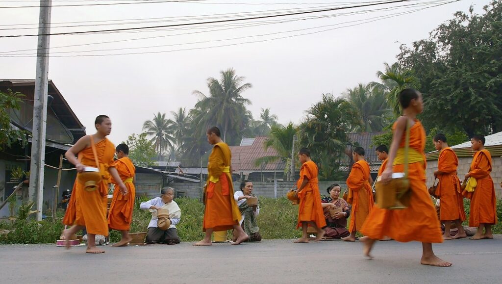 Laos: Monks in orange robes collect alms from locals. Buddhist tradition. Southeast Asia travel. Culture.