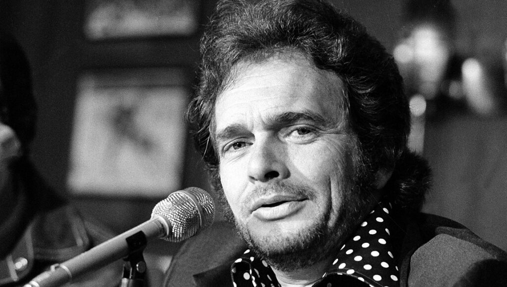 Black and white portrait of Merle Haggard singing into a microphone. Country music icon.