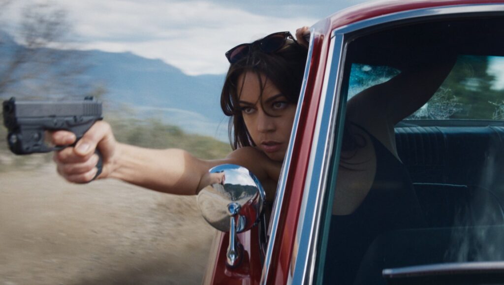 Aubrey Plaza in Operation Fortune. Woman in car aims gun. Action movie scene.