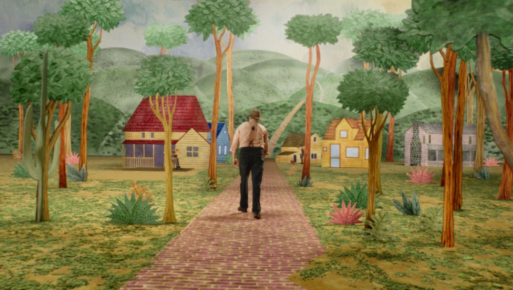 Beau Is Afraid movie scene. Man walking on a brick road through a whimsical, colorful cartoon forest. Houses in background.