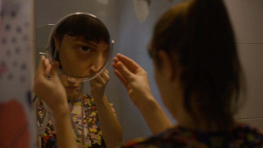 The Face of the Jellyfish film still. Woman looks in mirror, face reflected. NDNF 2023 film.