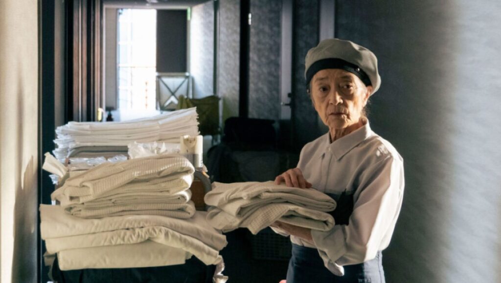 Plan 75 movie scene: Elderly woman worker with linens. Film still, drama.