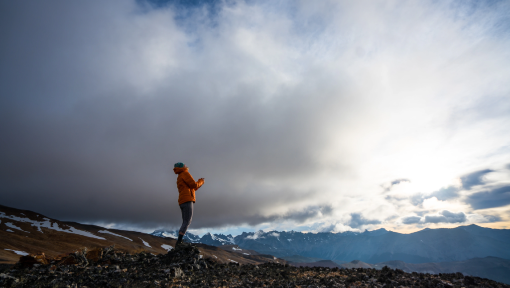 Woman hiking in mountains. Adventurer on rocky peak with scenic cloudy sky. Outdoor adventure and travel.
