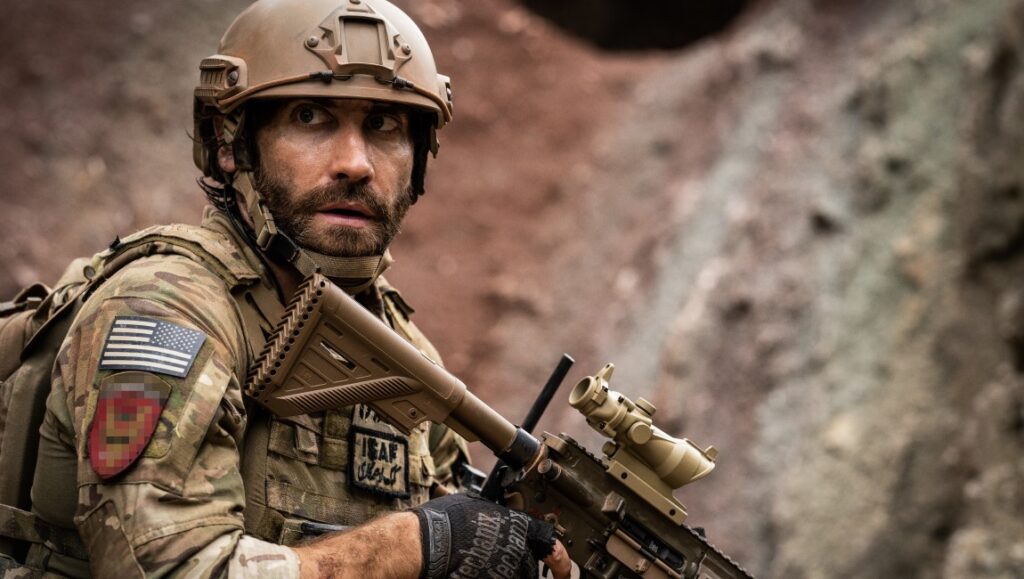 Jake Gyllenhaal in Guy Ritchie's The Covenant movie. Soldier in combat gear with rifle, looking alert.