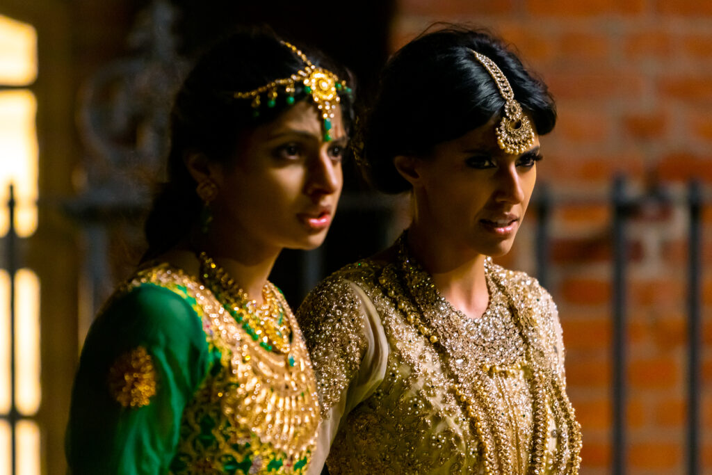 Polite Society film still featuring two women in traditional South Asian dresses and jewelry.