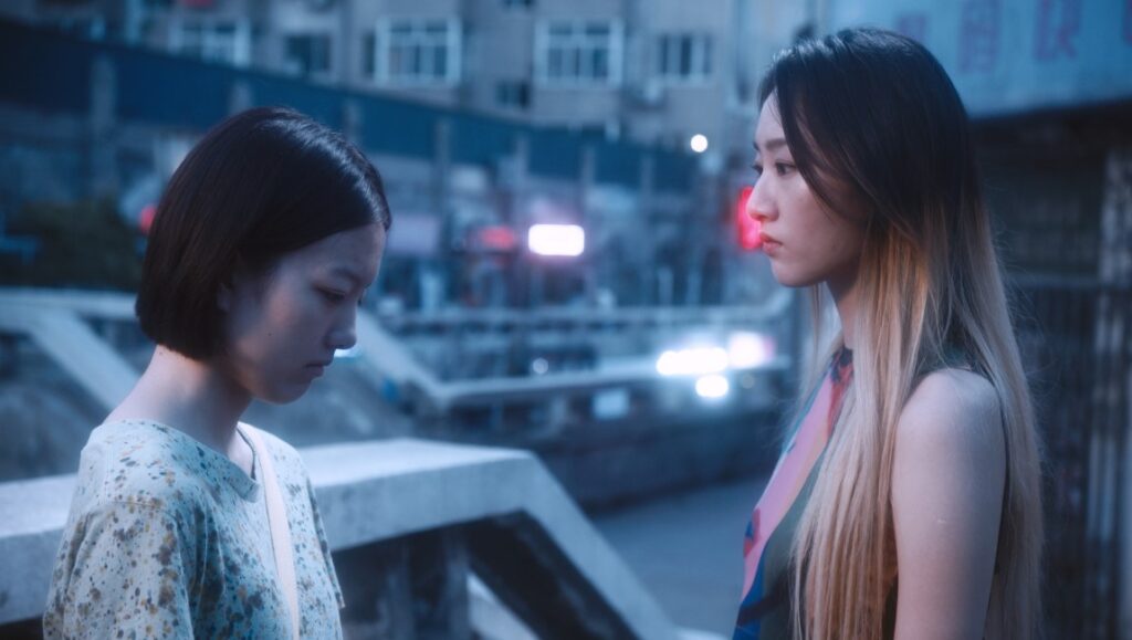 A Song Sung Blue film still: Two young women face each other in an urban setting. Cannes '23 review.