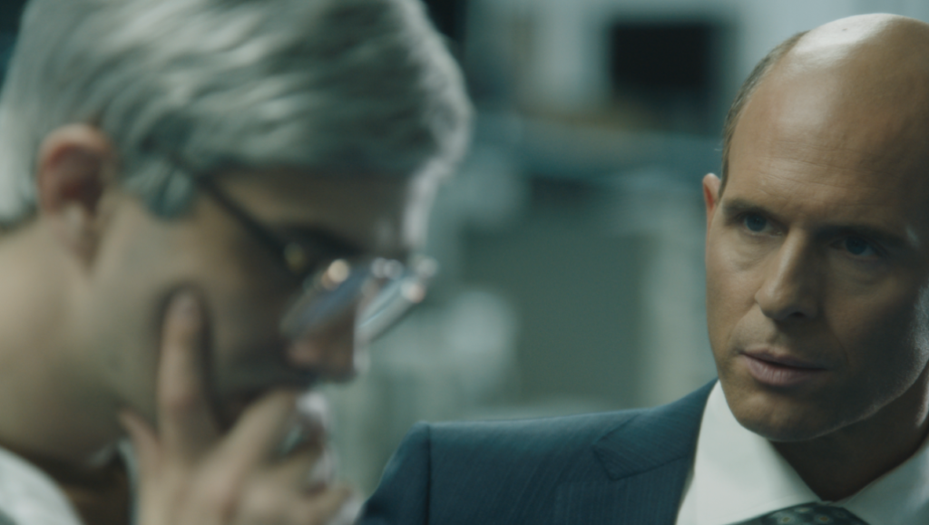 Film scene from Blackberry featuring two men in business attire. One is bald and in focus.