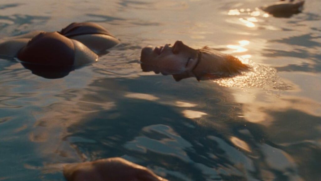 Person floating in water. Tranquil scene with golden sunlight reflecting on the water's surface. Serene, peaceful.